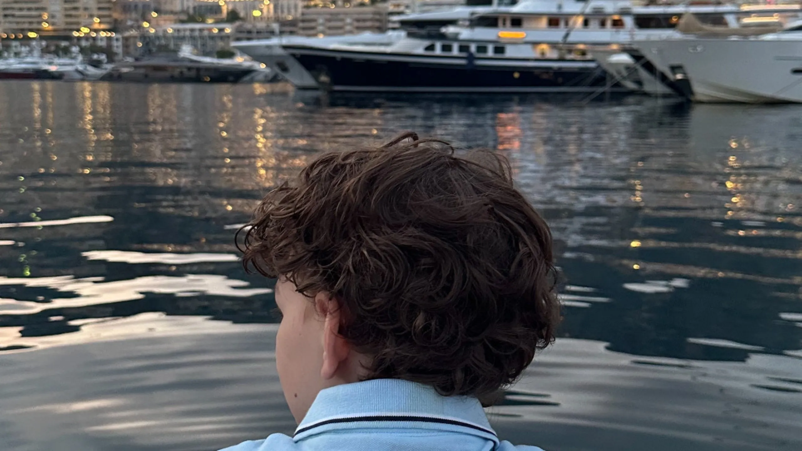 Ryan Rijvers seen from behind at the harbour in Monaco at dusk, looking out
over moored boats and the lit hillside beyond.